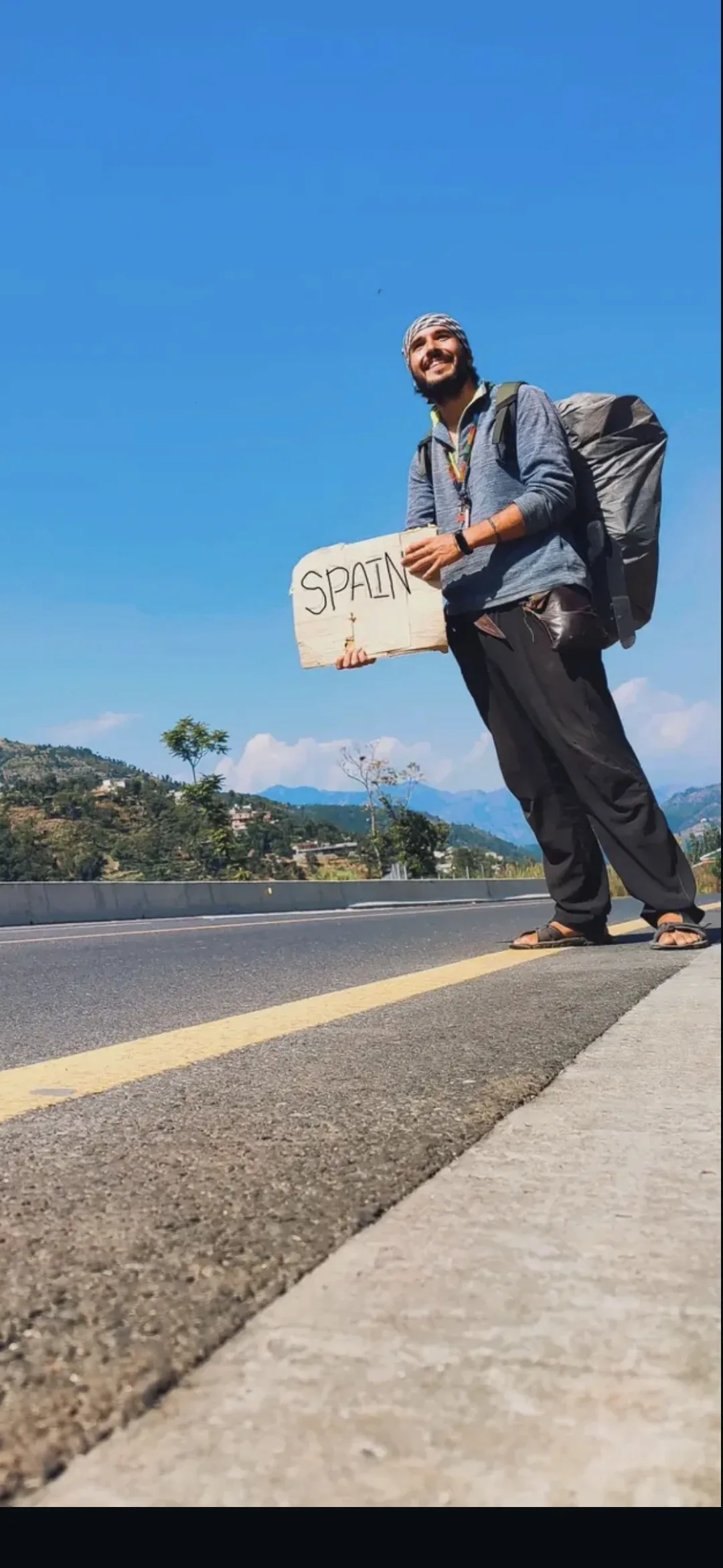 Carles haciendo autostop en una carretera con un cartel que indica SPAIN, durante su regreso por tierra desde la India